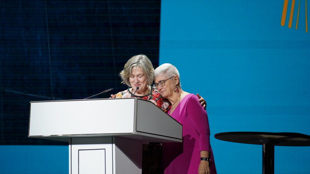 A picture of two people hugging on a stage behind a podium