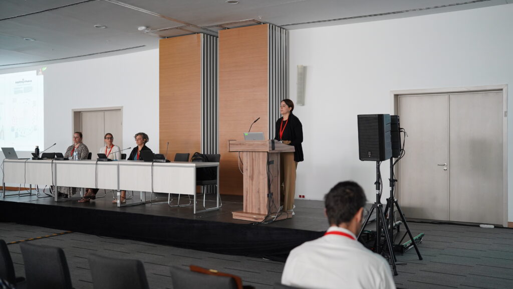 An image of a person standing behind a podium next to a table of people with speakers